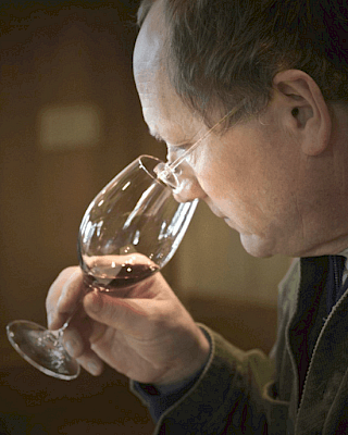 A person is closely smelling a glass of red wine, engaging in wine tasting or evaluation, indoors, focusing on the aroma.