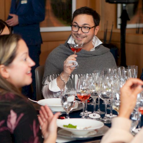 People sitting at a table with many wine glasses, engaged in conversation.