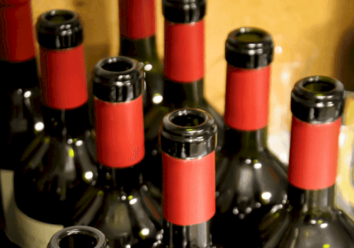 The image shows several wine bottles with red caps and necks, arranged closely together.