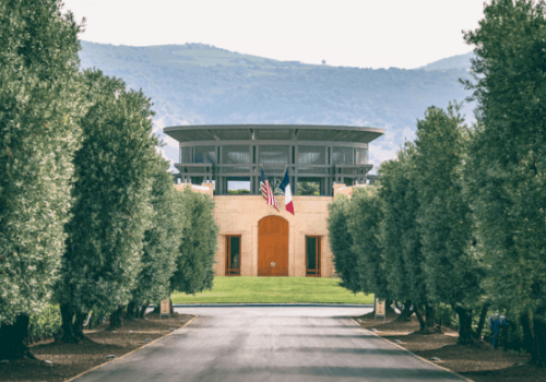 A modern building with U.S. and French flags, flanked by trees, set against a backdrop of green hills.