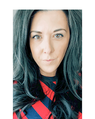 The image shows a person with long dark hair wearing a red and black checkered top against a light background, looking directly at the camera.