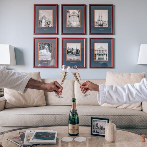 Two people clinking champagne glasses in a living room with art on the wall, a bottle on the table, and a cozy sofa.