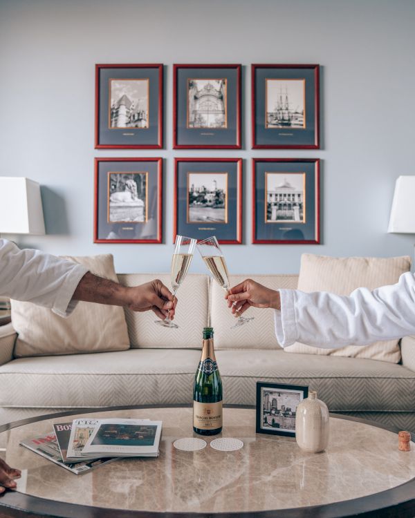 Two people clinking champagne glasses in a living room with art on the wall, a bottle on the table, and a cozy sofa.