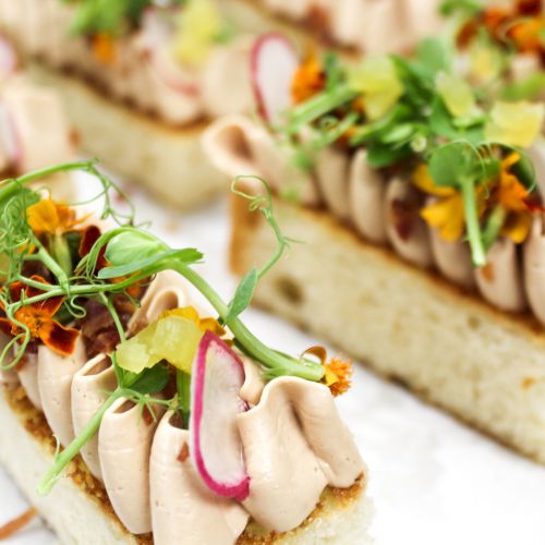 Gourmet canapés with whipped topping and garnished with herbs and microgreens on toasted bread slices, artfully arranged.