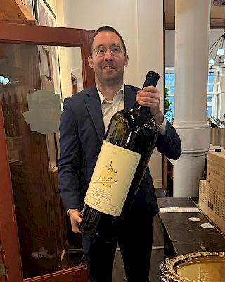 A person in formal attire holding a large wine bottle in an indoor setting.